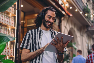 Smiling freelancer with tablet laughs while interacting outdoors, fully immersed in tech flow and...