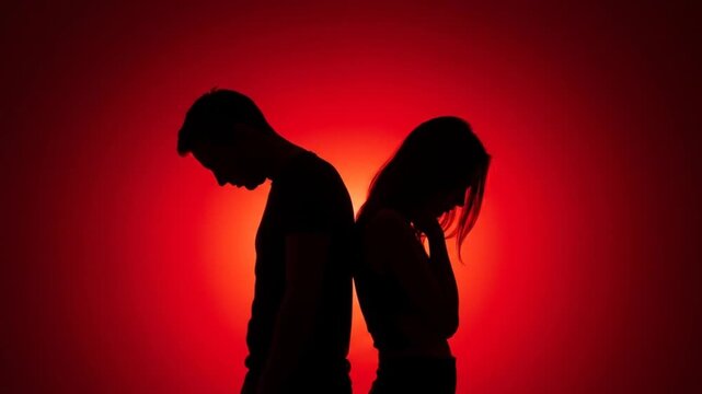 Silhouetted couple back to back, with heads bowed, against a vibrant red gradient