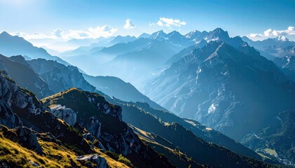A vast, layered mountain landscape under a clear blue sky, with sunlight illuminating the foreground and distant peaks shrouded in atmospheric haze.