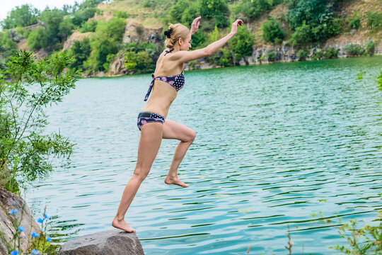 Young happy woman having fun jumping in lake from cliff. Young woman jumping into lake from rock, summer fun and adventure