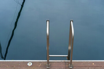 Metal handrail for descent into the lake, pier on the lake and calm lake water on background