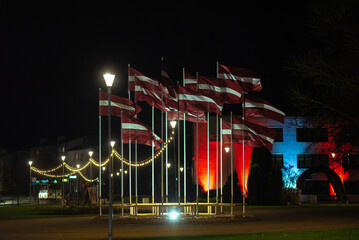Latvian flags waving at night with festive lights and illuminated buildings creating a patriotic and atmospheric city scene.