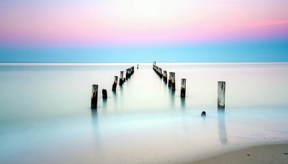 A tranquil seascape featuring a line of old wooden pilings receding into the calm ocean water, set against a soft pastel sky.