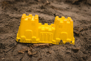 Colorful yellow sandcastle standing alone amidst sandy terrain in a playful summer scene