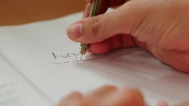 Hand and Pen writing the August cover page of bullet journal notebook monthly spread - close-up static shot