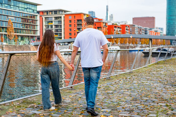 Happy young couple, happy girl and man together, shared journey, planning, waterfront promenade, modern apartment buildings, and considerations, intimate moment in urban landscape, cheerful dreams