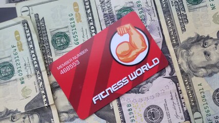 Detailed close-up shot of a red fitness membership card placed on a spread of US dollar bills. Rich texture and vibrant colors make this scene perfect for concepts of finance, fitness, and membership.