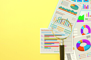 Magnifying glass on business data charts and graphs. Data analysis, financial audit, and marketing report concept. Business Intelligence (BI) on yellow background with copy space.
