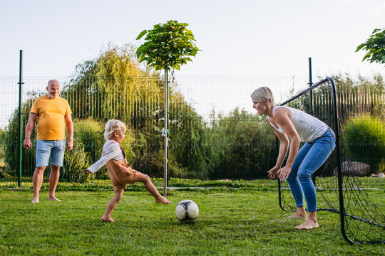 Little boy playing football with mother and grandfather in backyard. - Powered by Adobe