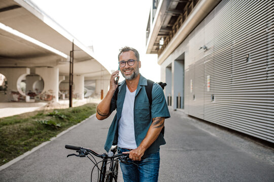 Male cyclist making phone call, standing by his bike.