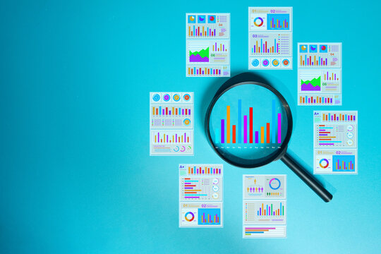 Magnifying glass analyzing business data charts and graphs. Data analysis, financial audit, and marketing research concept. Blue background with copy space.