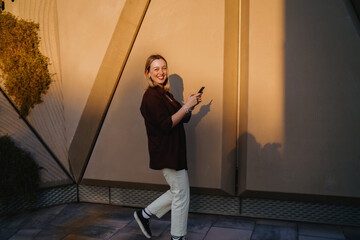 Smiling woman walking with smartphone, turning towards camera with joyful expression, representing positive digital lifestyle, online engagement and mobile communication.