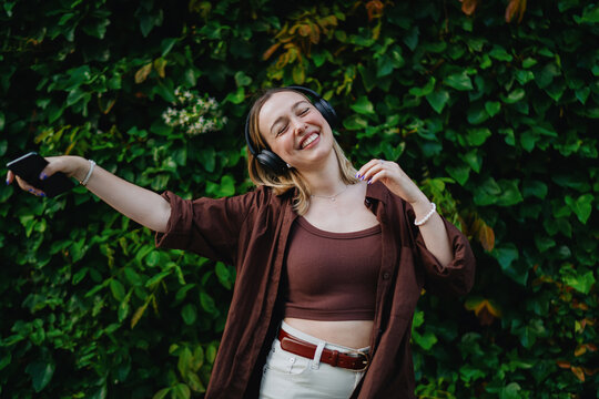 Young woman with skateboard at side, smartphone in hand, head tilted slightly, generously embodying balance between analog mobility and digital presence.