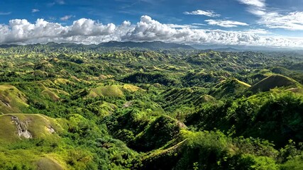 Aerial view of a lush, rolling green landscape under a vibrant blue sky filled with puffy white clouds