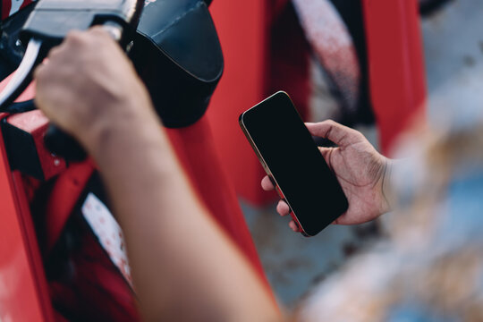 Hand holding smartphone next to red rental bike, concept of technology enabling eco-friendly transportation. Stock photo symbolizing app-driven urban lifestyle and digital mobility.