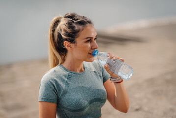 Young sporty woman drinking water from plastic bottle after training outdoors