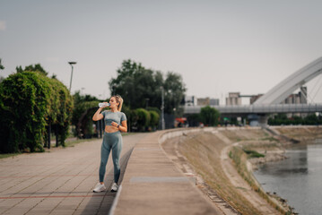 Obraz premium Young sporty woman drinking water after training outdoors by the river