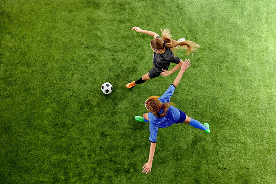 Female soccer players competing for ball in fast offensive clash on grass field. Concept of competition, adrenaline and determination during high-speed match movement.