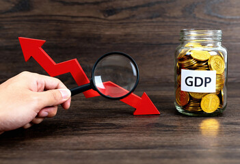 Gross domestic product GDP analysis with magnifying glass on red chart indicating decline and gold coins in jar on wooden table