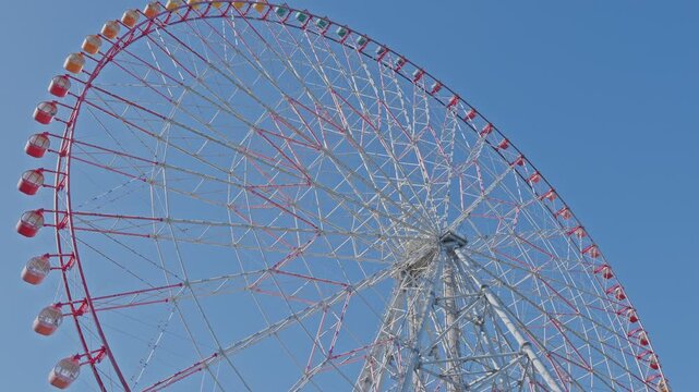 A dynamic close-up of the massive Ferris wheel at Kasai Rinkai Park (Diamond and Flower Ferris Wheel), with its vibrant red and white structure against a clear blue sky.