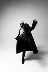 A person strikes a playful pose in a stylish coat, playfully lifting their foot