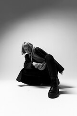A model crouches dramatically on a light backdrop, wearing a modern outfit that highlights street fashion. The mood is edgy, emphasizing the model's confident expression and stance