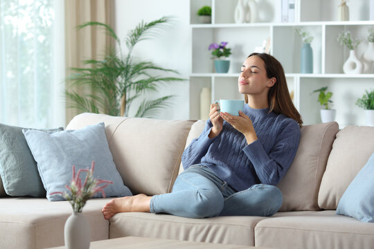 Relaxed woman in blue smelling coffee aroma at home