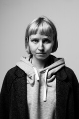 A young individual stands confidently against a plain backdrop, their serious expression revealing a mix of strength and vulnerability