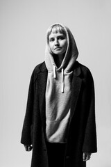 A person stands in a modern studio, exuding confidence with a relaxed expression. Dressed in a comfortable hoodie and long coat, they embody casual style against a soft backdrop