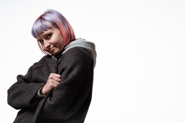 A young woman showcases her vibrant hair colors and unique style while posing confidently in a simple indoor space. She wears a warm coat over a hoodie, emphasizing comfort and self-expression