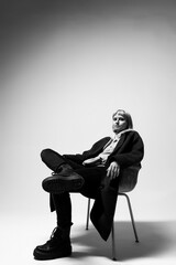 A person sits confidently in a modern chair, dressed in stylish black attire. The stark background enhances the feeling of calm and introspection in the early afternoon light