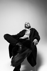 A fashion-forward person sits confidently in a minimalist studio. Wearing a cozy hoodie and oversized coat, they exude a powerful aura while displaying edgy boots and a relaxed posture
