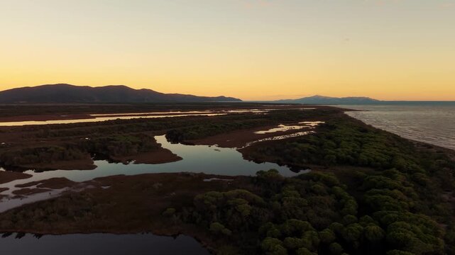 Peaceful reflections of sunset clouds in lagoon water at Parco Maremma coast seaside. Tuscany aerial