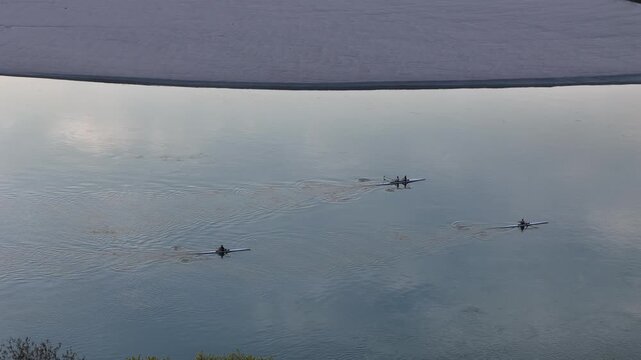 Rowing boats from Cremona-based teams training on Po River, Lombardy, Italy, with synchronized movement under golden sunset light, highlighting local sporting culture and river-based athleticism.