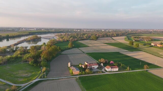 Po River flowing between Lombardy and Piacenza province, Italy, with structured agricultural fields, scattered farm buildings, and tree-lined banks typical of the Padana plain&rsquo;s rural landscape.