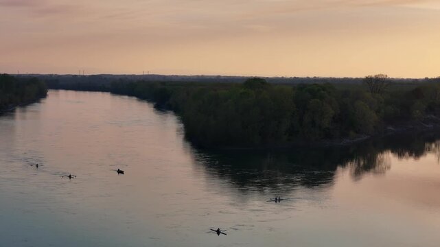 Rowing boats from Cremona-based teams training in the Maginot bodri zone near Olza, Castelvetro Piacentino, Italy, gliding across calm Po River waters under sunset light