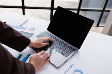 Business professionals collaborate at a desk, analyzing financial reports and data on a laptop. They use charts and graphs to discuss trends and insights in a modern office setting
