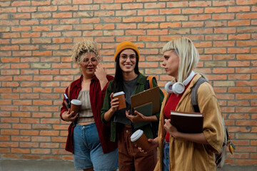 Young women students walking and talking outdoors with coffee