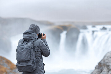 Adventurer capturing a powerful waterfall. Solitude, exploration, and the beauty of nature. Inspiring wanderlust, perfect for travel or outdoor themed projects.