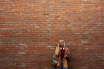Young woman smiling talking on phone against brick wall