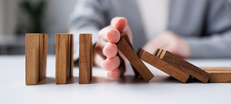Woman stopping wooden blocks from falling on desk background, Domino effect planning strategy of project management.
