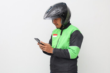 Asian online taxi driver with green jacket and helmet standing while using cell phone. Isolated on white