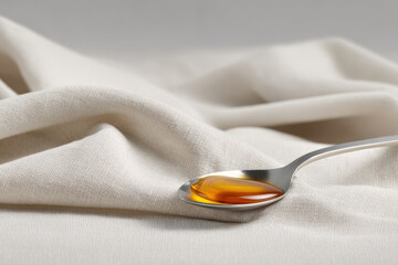 single drop of honey elegantly rests on gleaming spoon surrounded by soft linen backdrop