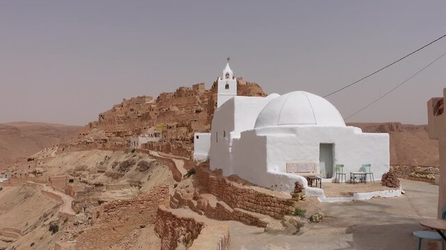 Walking towards white mosque in Berber town of Chenini, built on spectacular mountain ridge in Tunisia
