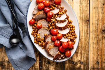Roast pork tenderloin served with chickpeas and tomatoes in plate