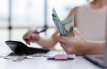 Close up of business woman is calculating for payment finances and holding dollar managing domestic budget and calculating taxes using calculator and laptop