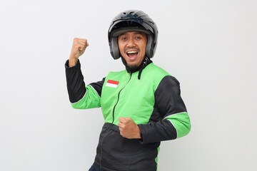 Successful Asian online taxi driver with green jacket and helmet showing winning gesture with clenching fist