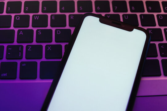 Stylish top view close up of smartphone lying on laptop keyboard with neon lighting, minimal mockup for app presentation. Copy space for digital ad or creative template.