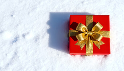 Red gift box with golden bow on white snow background. Simple holiday layout.