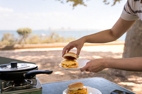 Woman camping and preparing a burger by the sea